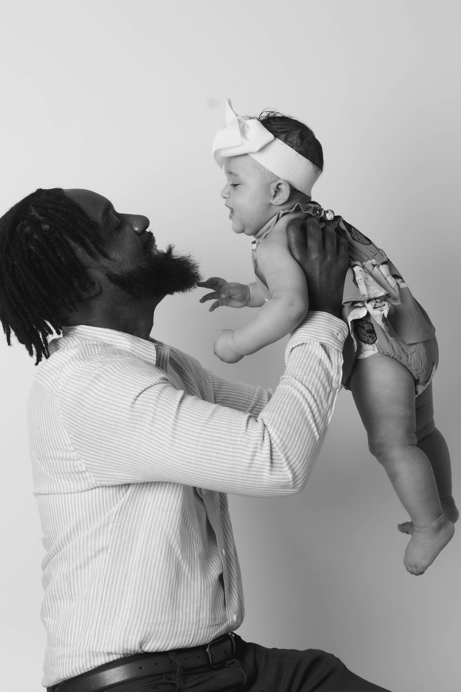 Black and white photo of proud father lifting his baby girl overhead in a joyful moment.