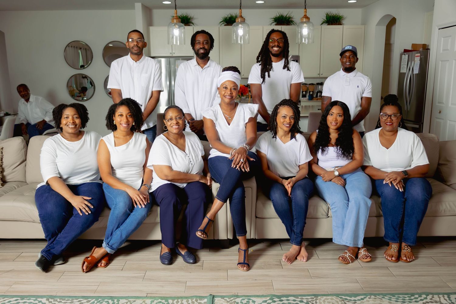 Large family group portrait in matching white tops and jeans posed in modern living room.