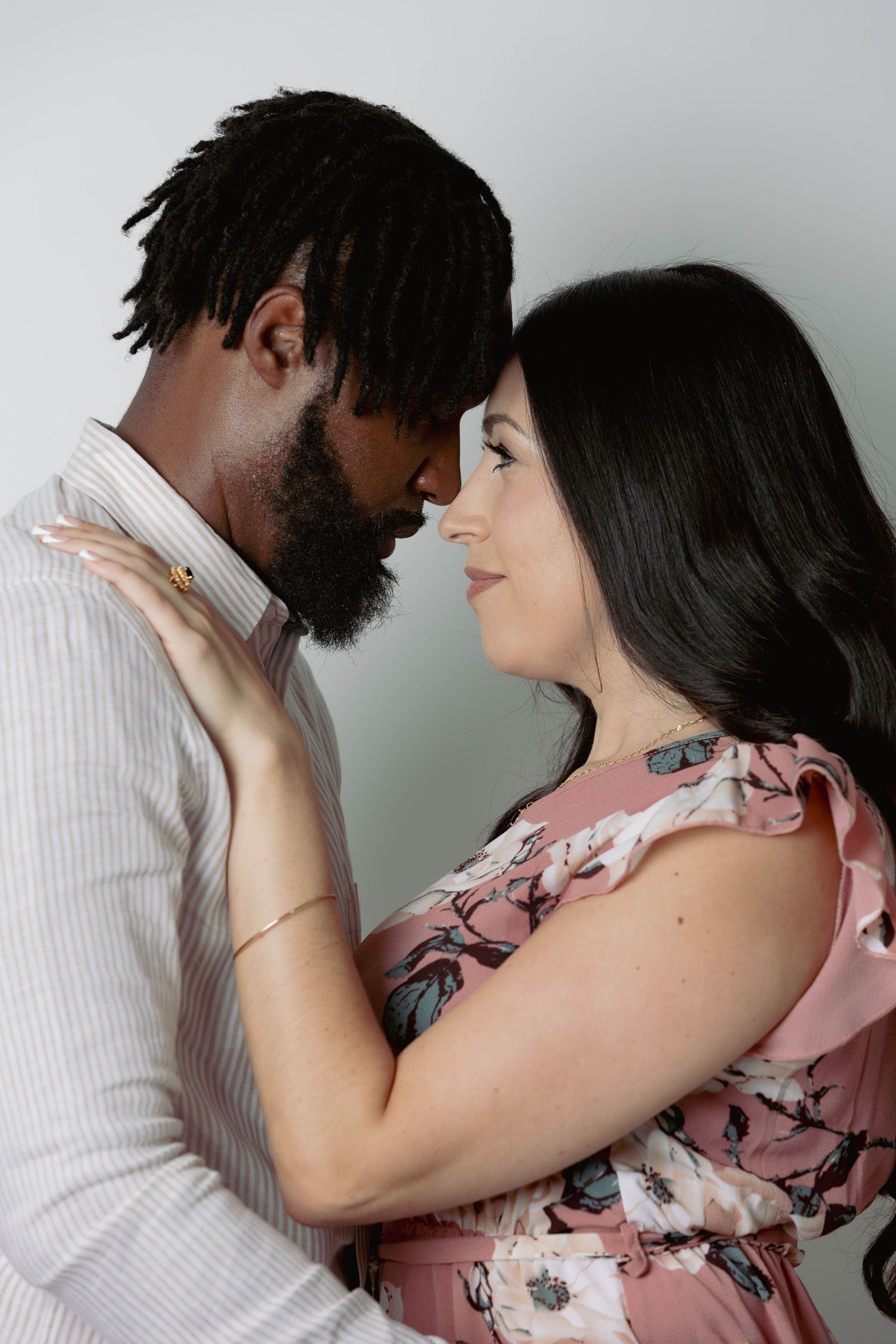 Intimate couple portrait with foreheads touching, man in striped shirt and woman in pink floral dress.