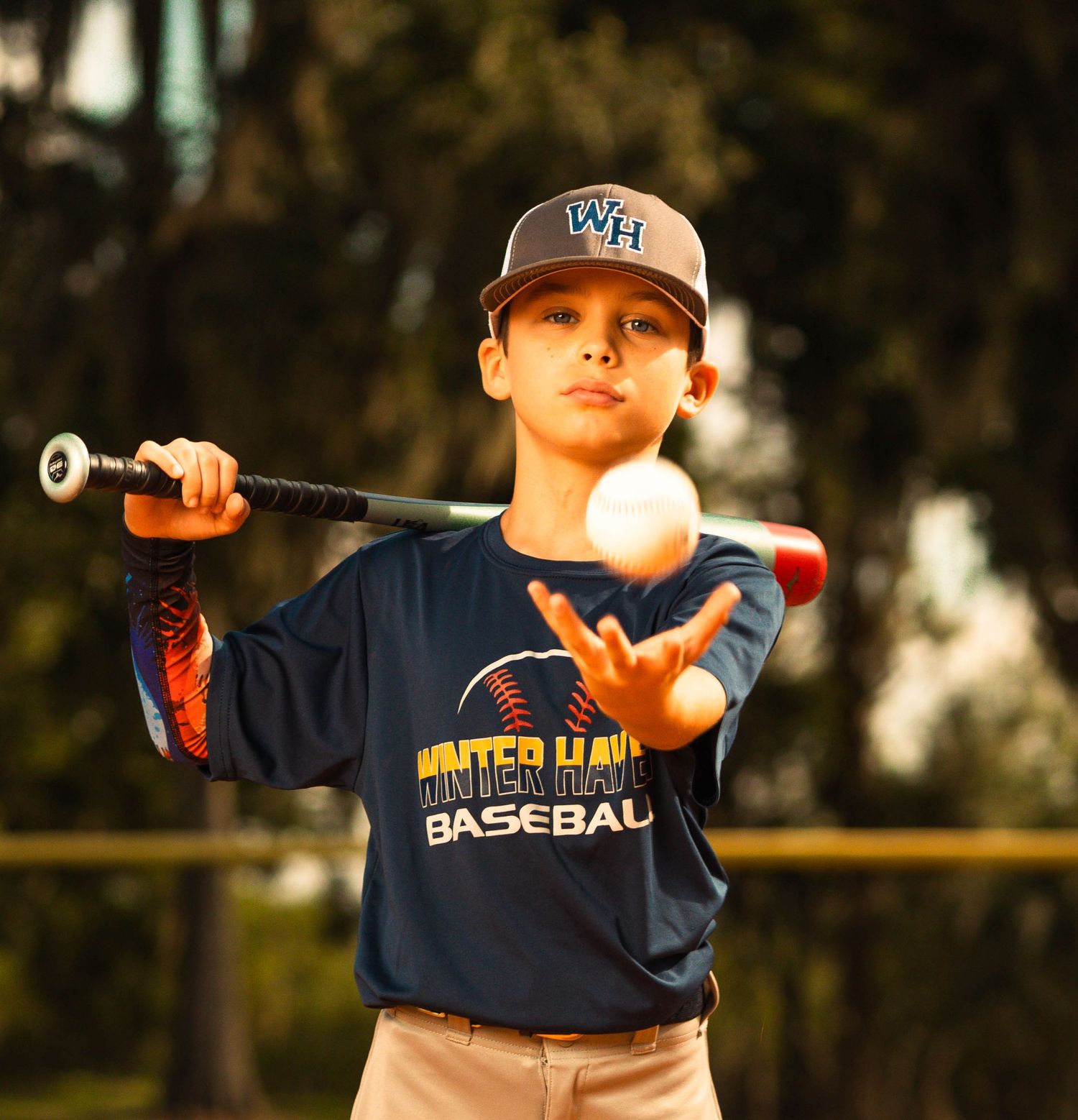 Young baseball player in Winter Haven Baseball uniform tosses a ball outdoors during practice.
