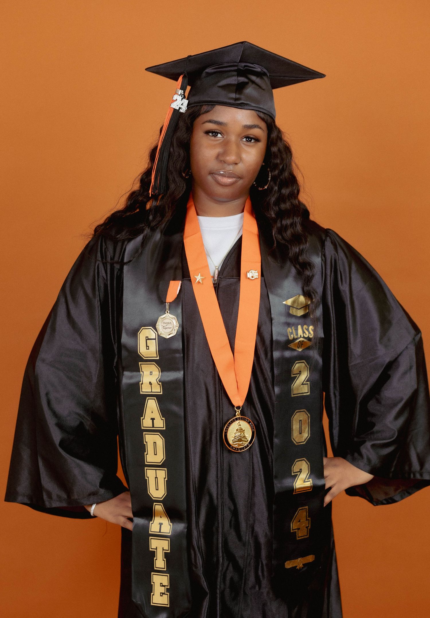 Proud graduate posing in black cap and gown with Class of 2024 stole and gold medal.