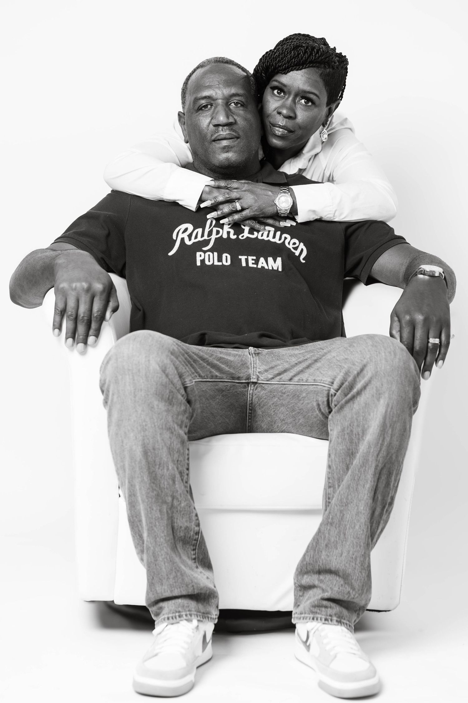 Black and white portrait of couple posing together, man seated in white chair.