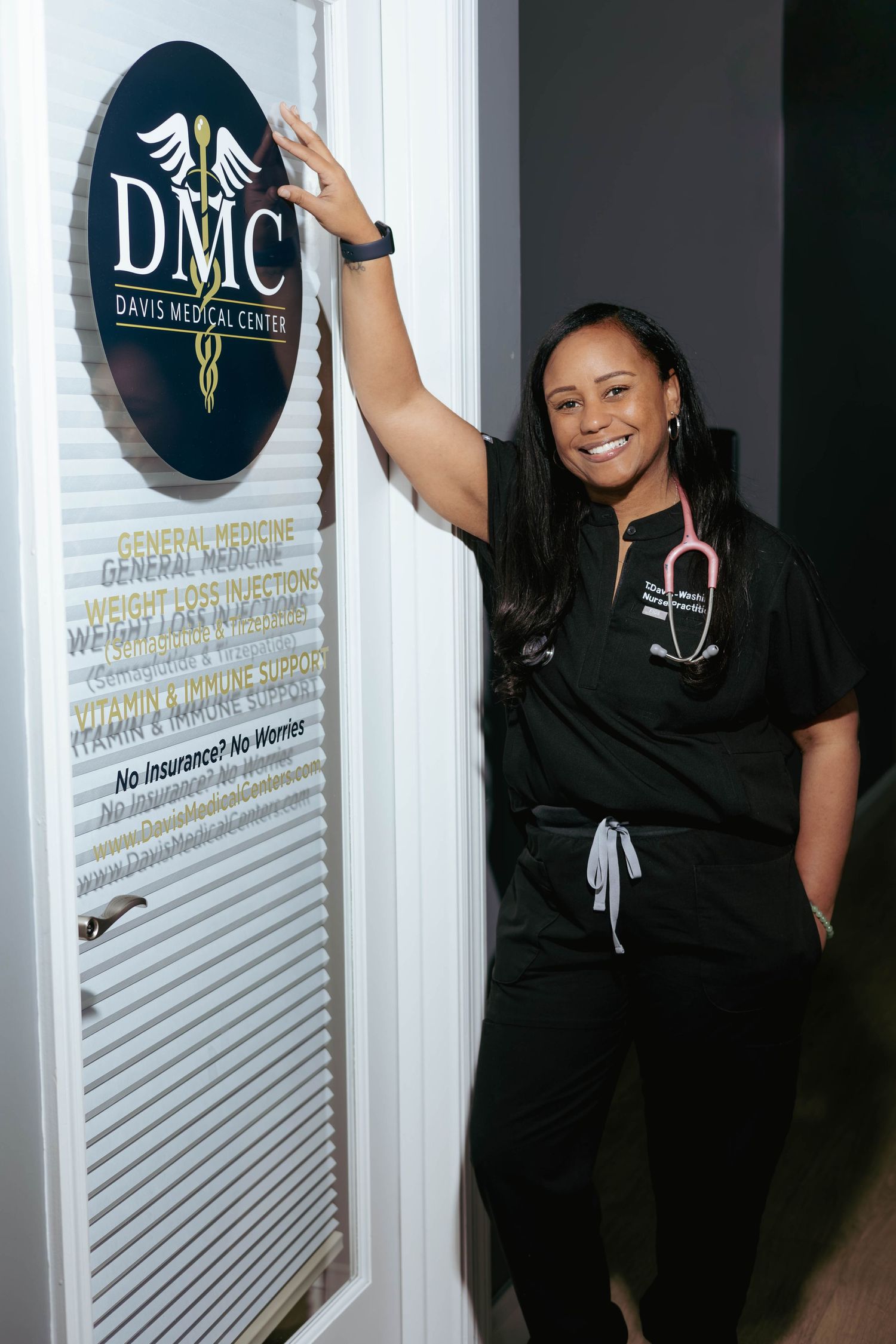 Smiling Black female nurse in scrubs posing at Davis Medical Center entrance door.