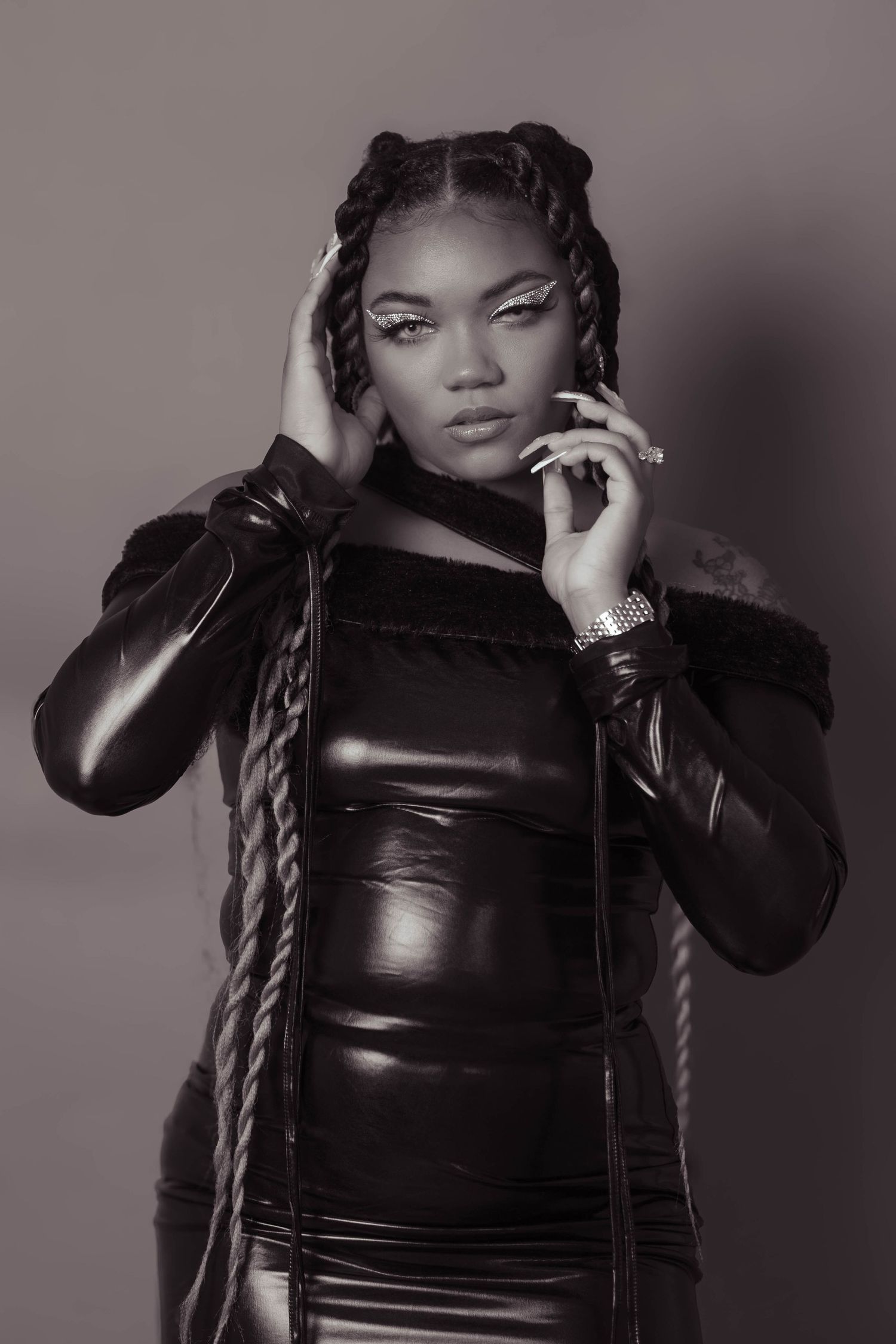 Black and white portrait of young woman in latex outfit with braids and bold makeup.