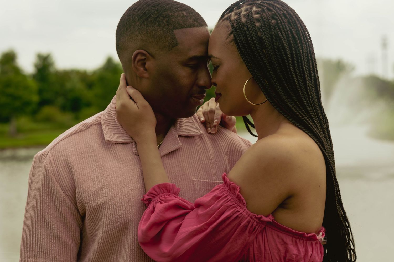 Romantic couple sharing an intimate moment outdoors near a fountain, dressed in pink and red outfits.