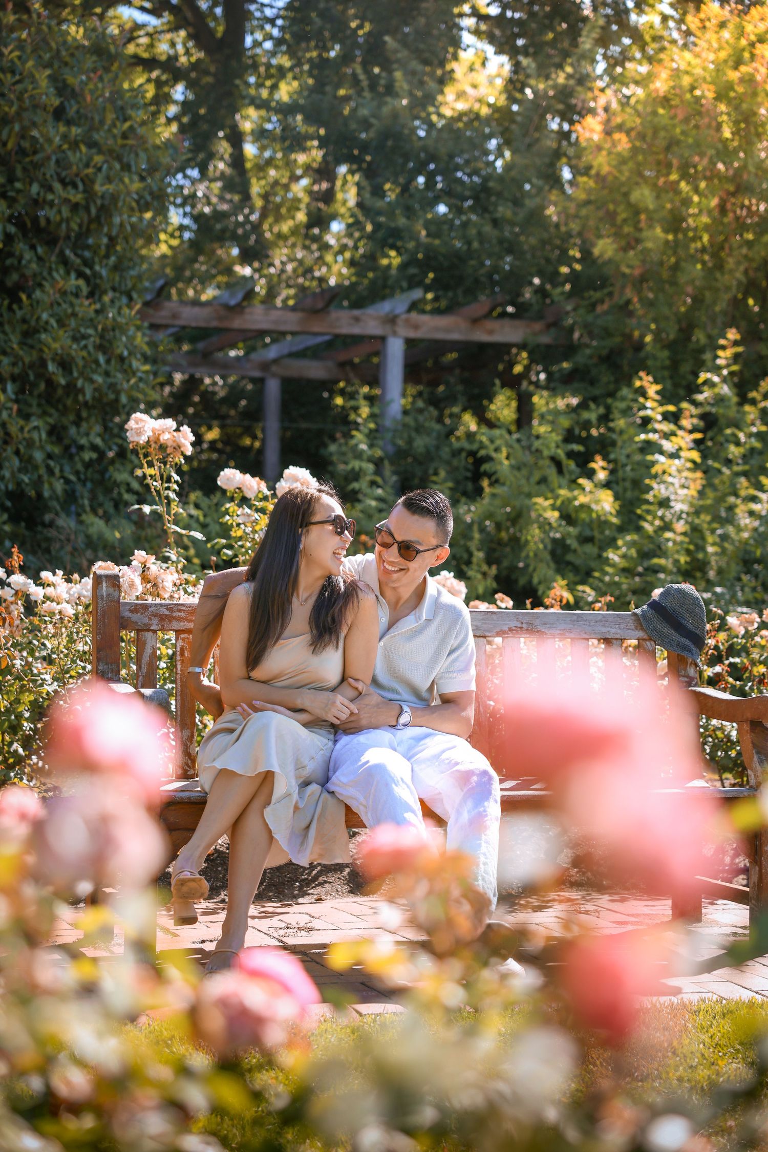 Intimate moment captured on a wooden bench in a rose garden with soft pink blooms.