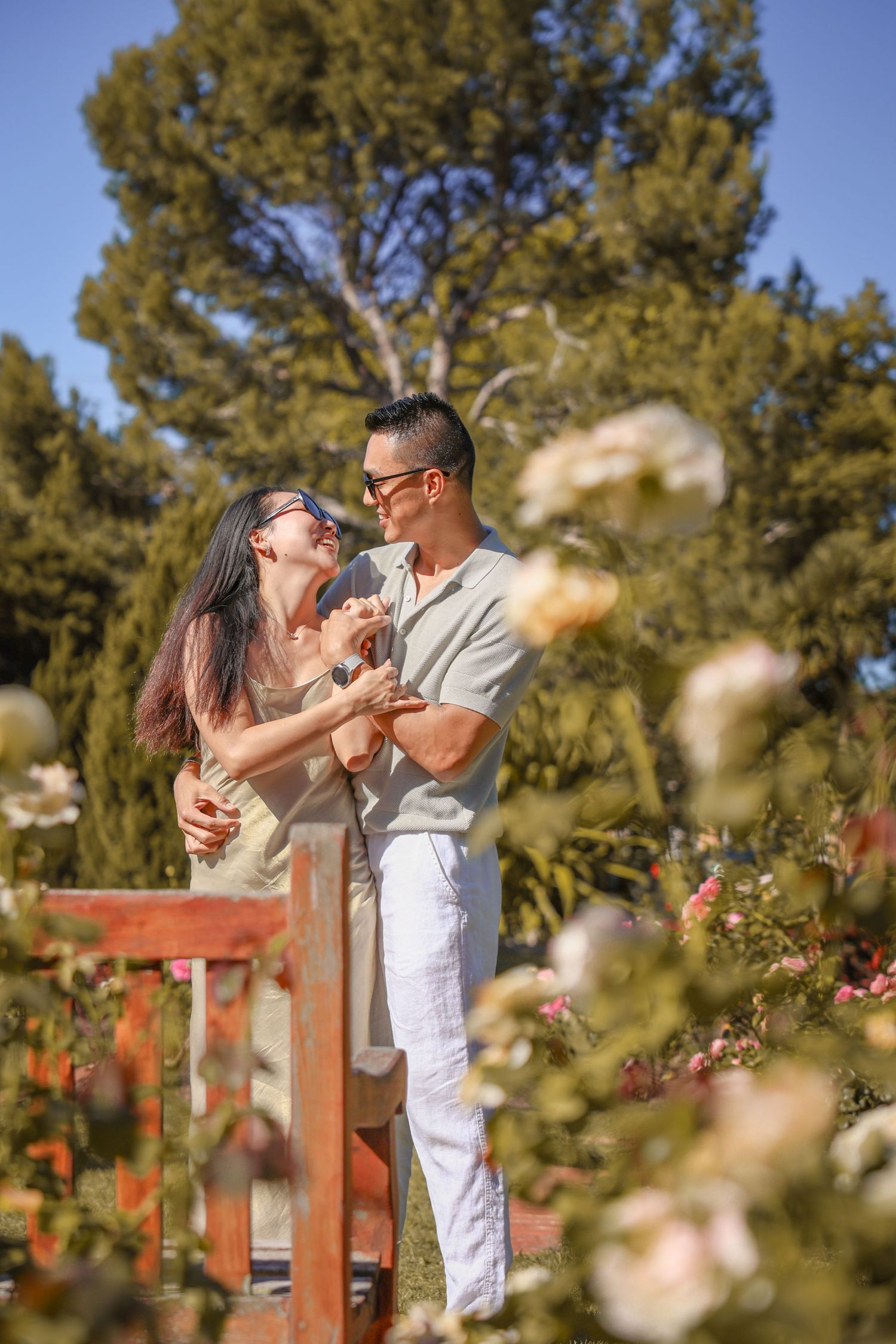 Romantic dance moment on a wooden deck surrounded by blooming roses and pine trees.
