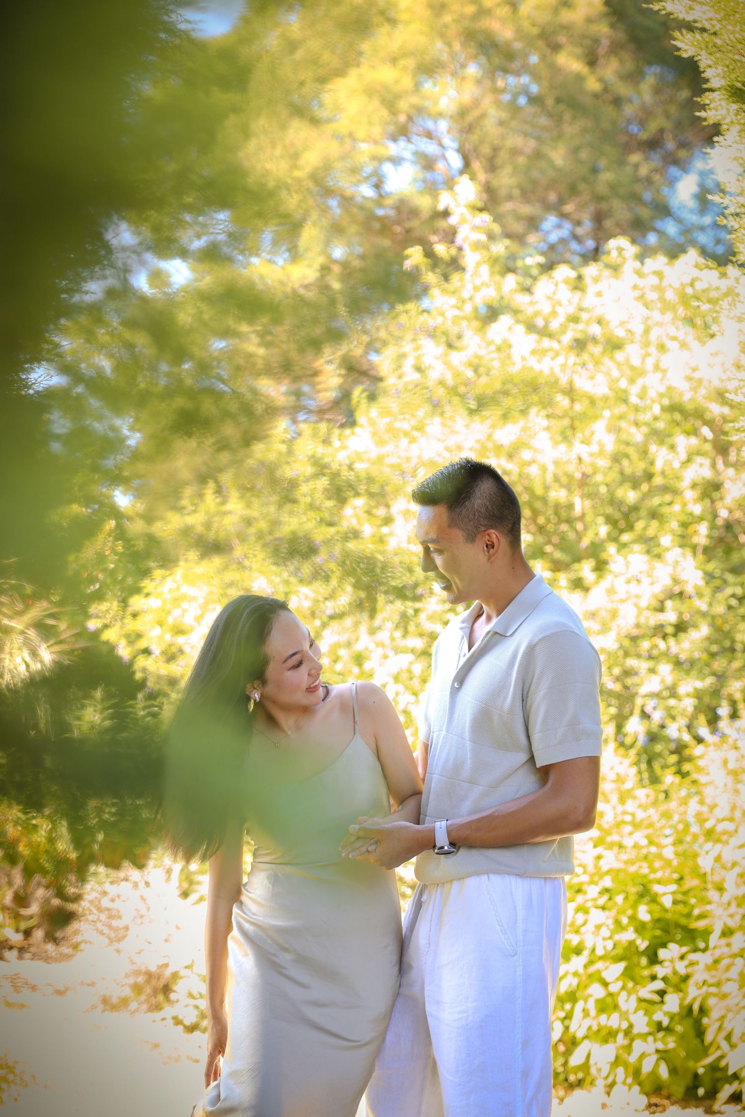 Romantic moment photographed through leaves with golden sunlight creating dreamy atmosphere.