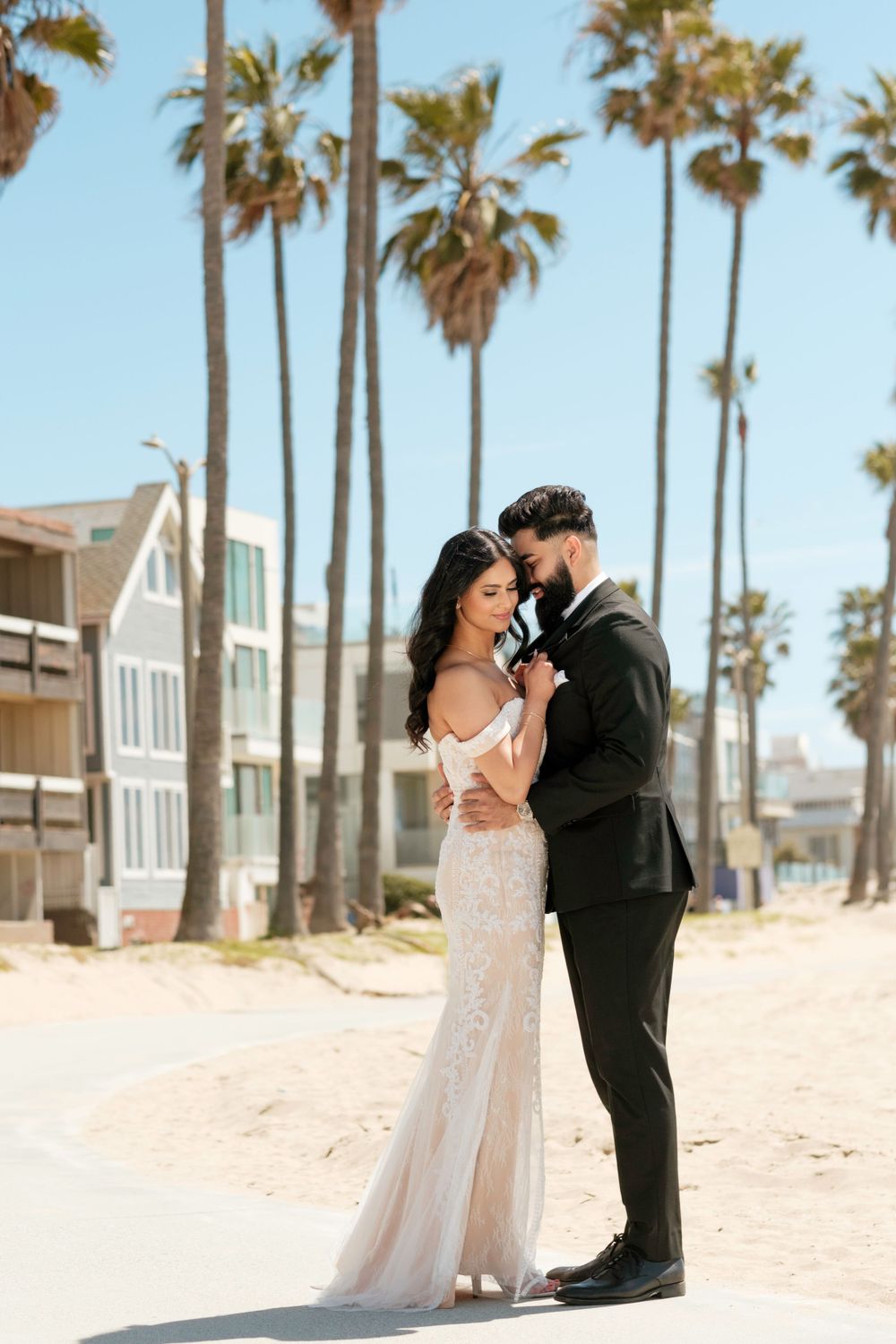 A romantic wedding couple embraces on a beach lined with tall palm trees in Southern California.