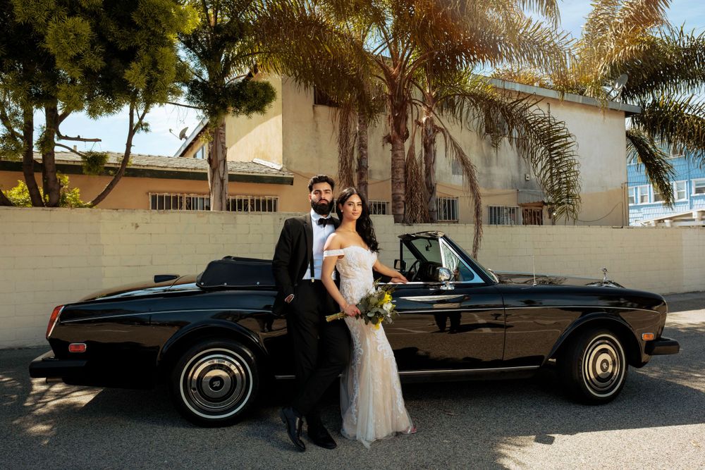A vintage black Rolls Royce convertible parked in front of palm trees on a sunny day.