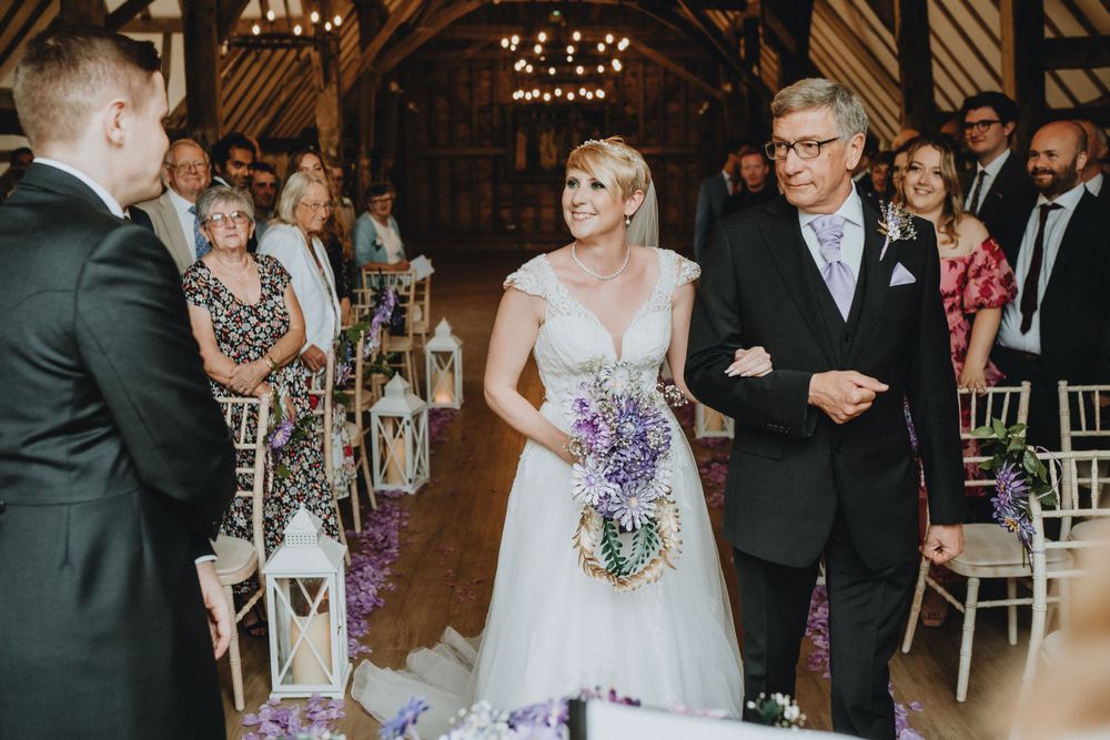 A traditional wedding ceremony takes place in an elegant barn venue with chandeliers and wood beam ceilings.