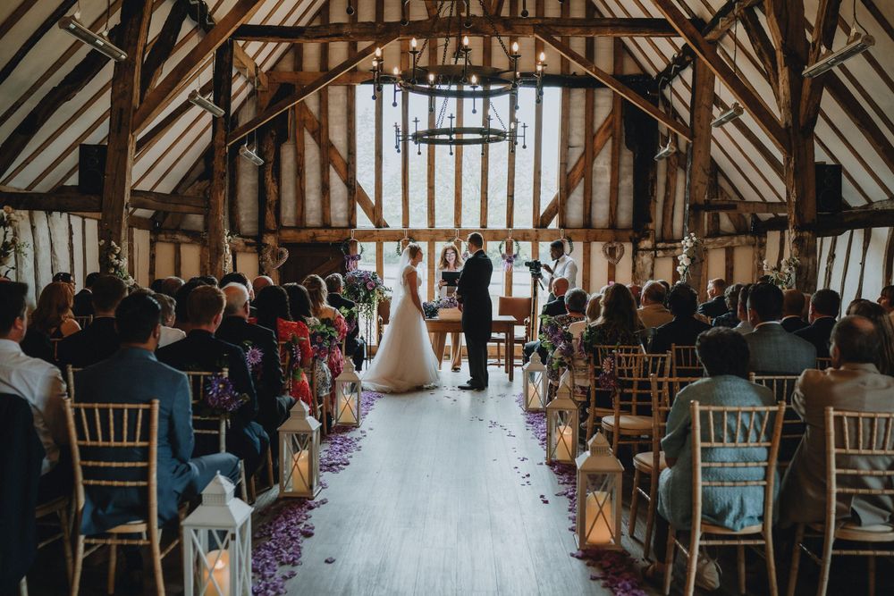 A rustic barn wedding ceremony at Colville Hall with exposed wooden beams, lanterns along the aisle, and guests seated in chiavari chairs.