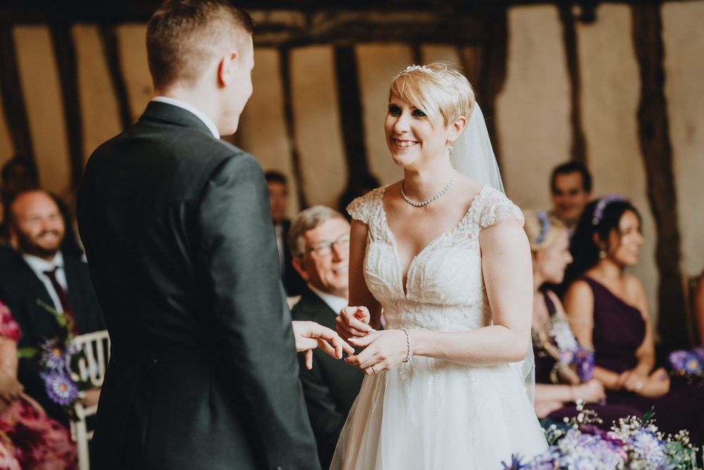 A joyful wedding ceremony moment between the bride and groom while exchanging rings indoors.