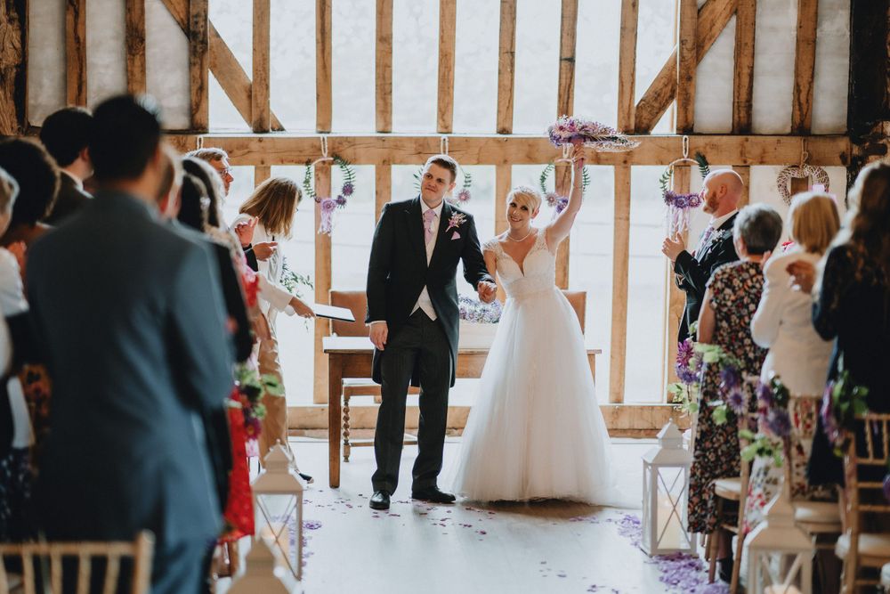 Couple celebrates joyfully during their barn wedding ceremony as guests look on and applaud.