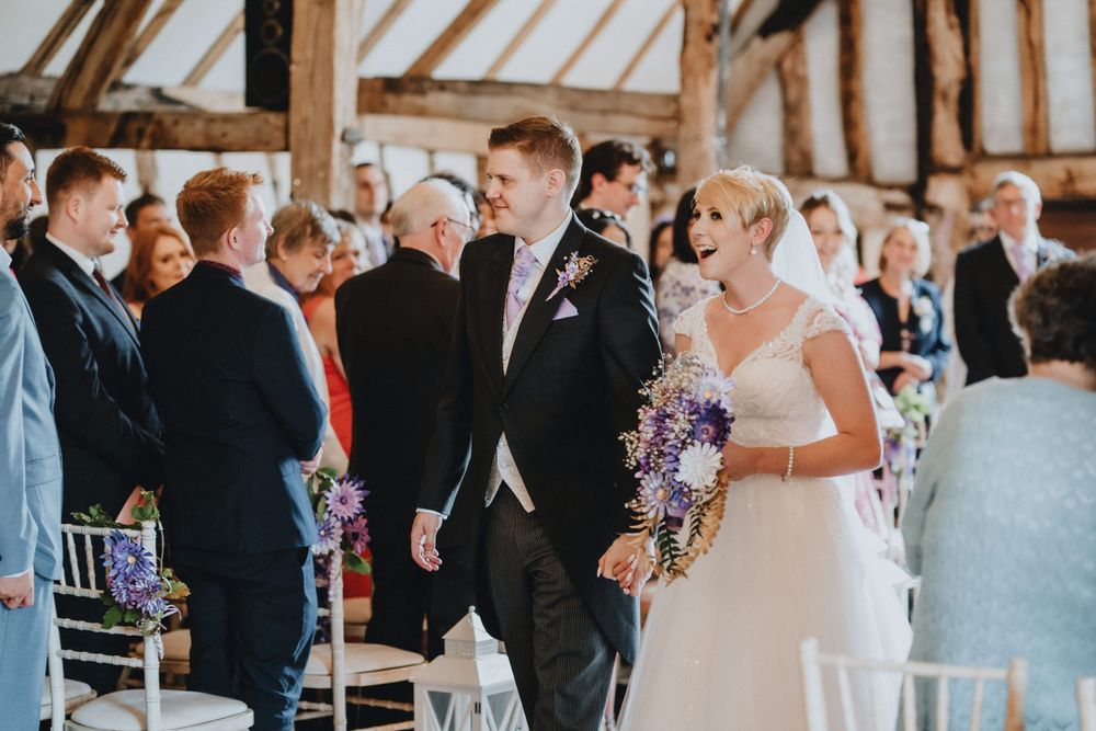 Wedding ceremony inside a rustic timber barn with guests gathered around as couple walks down the aisle.