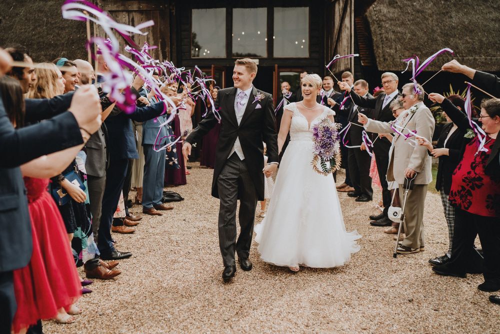 Wedding couple walks through grand exit with guests holding ribbon wands along the path at Colville Hall.