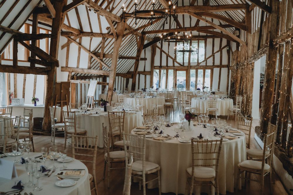 Elegant rustic barn wedding reception at Colville Hall with exposed wooden beams, white decor and round tables set for dinner service.