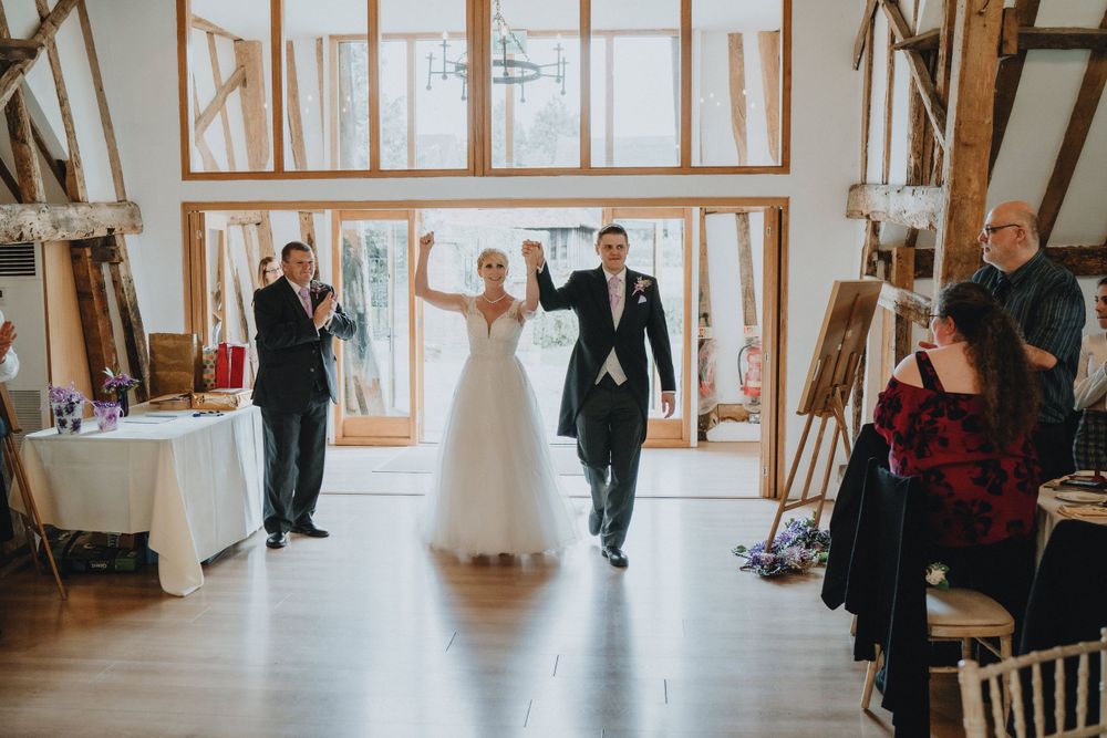 Guests celebrating at a rustic barn wedding venue with tall windows and wooden beams during a reception entrance.