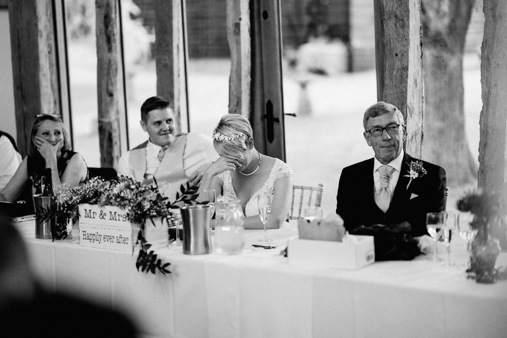 Wedding party guests share a candid moment of laughter at the head table during reception celebration in black and white.