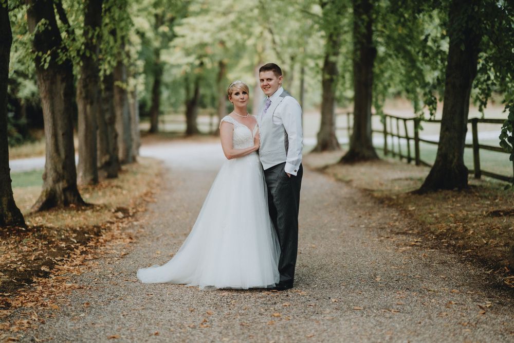 A couple stands together on a tree-lined path surrounded by lush greenery on their wedding day.