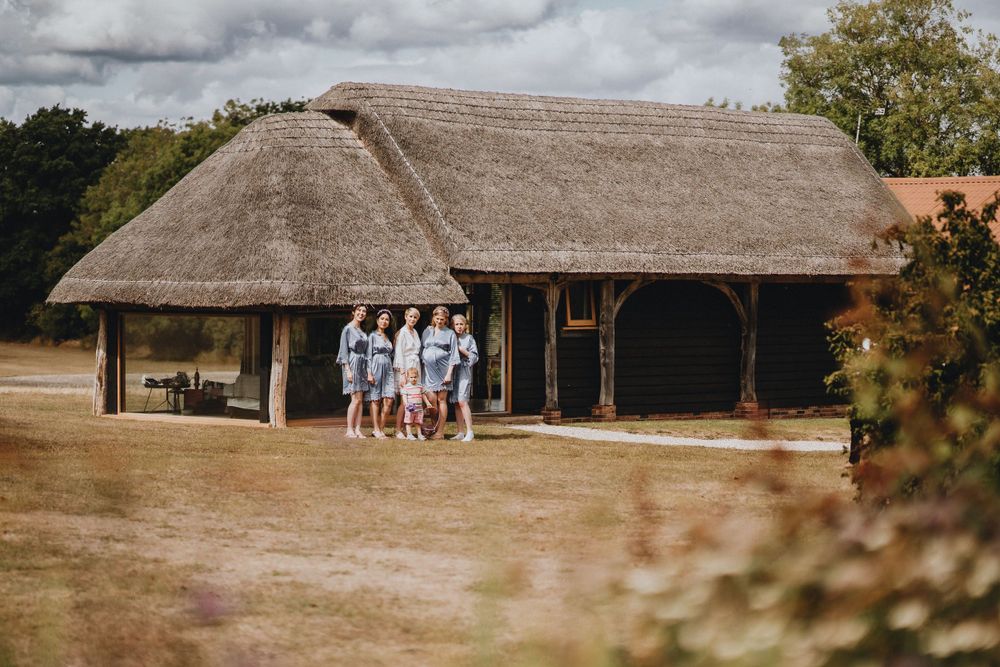 A traditional thatched-roof barn building at Colville Hall with a group of people standing under its rustic wooden frame structure.