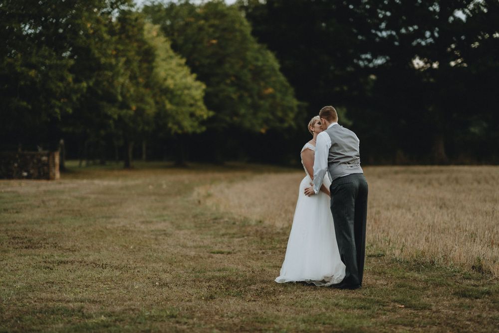 A couple embraces in a grassy field during a rustic outdoor wedding photoshoot at dusk.