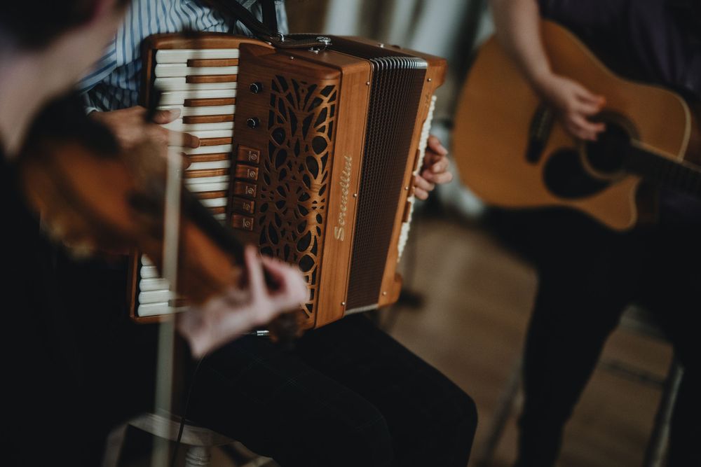 Musicians perform with an accordion and acoustic guitar in a dimly lit setting during a folk music performance.