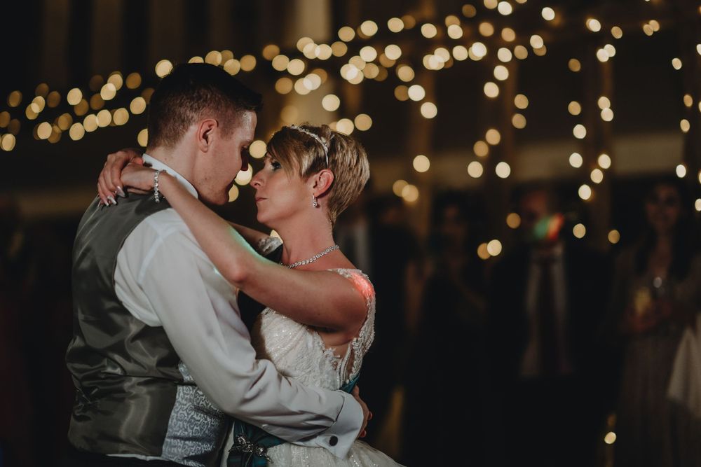 Romantic couple dances during wedding reception with twinkle lights creating magical ambiance in dark room.