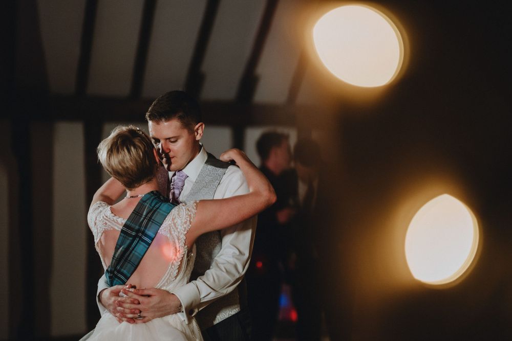 A couple shares a tender moment during their first dance at a wedding reception with warm glowing lights in the background.