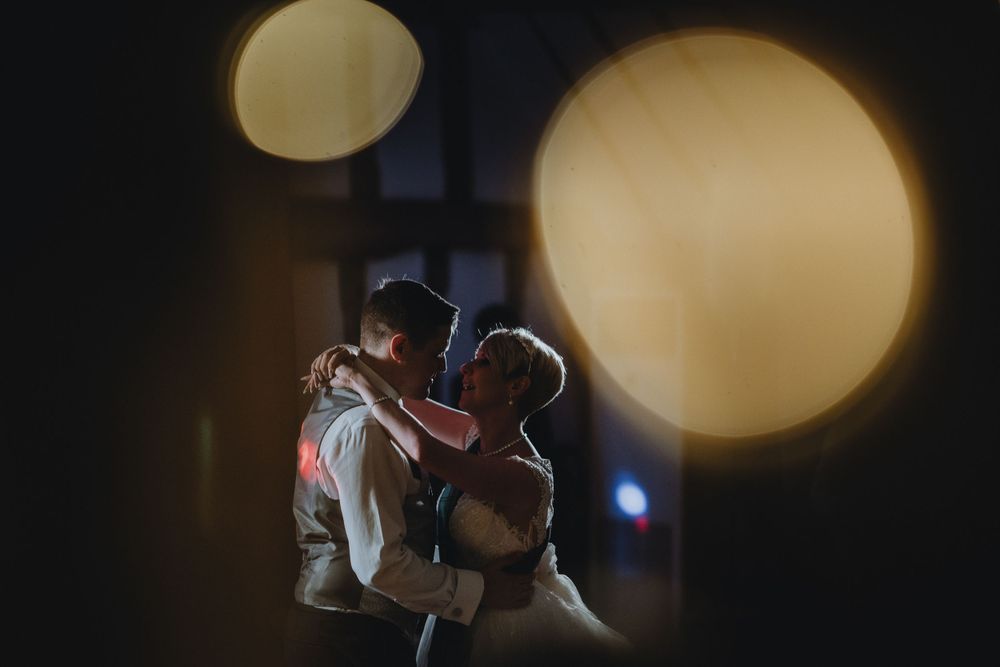 Two people embrace in a romantic dance pose with warm glowing orbs of light in a dark, atmospheric setting.