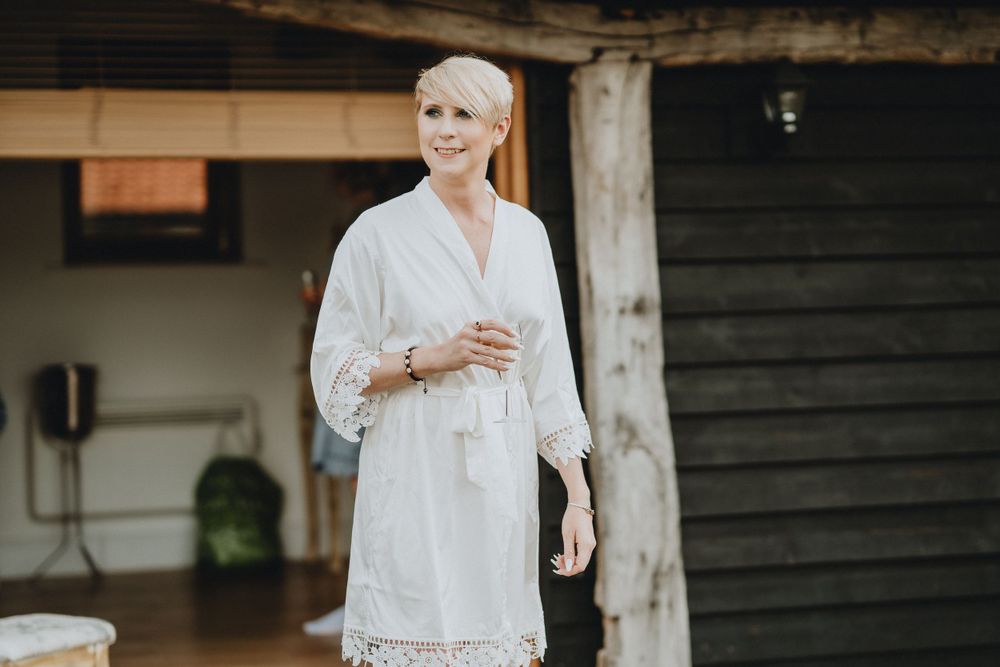 Someone wearing a white lace dress with batwing sleeves poses against a rustic wooden backdrop while holding a drink.