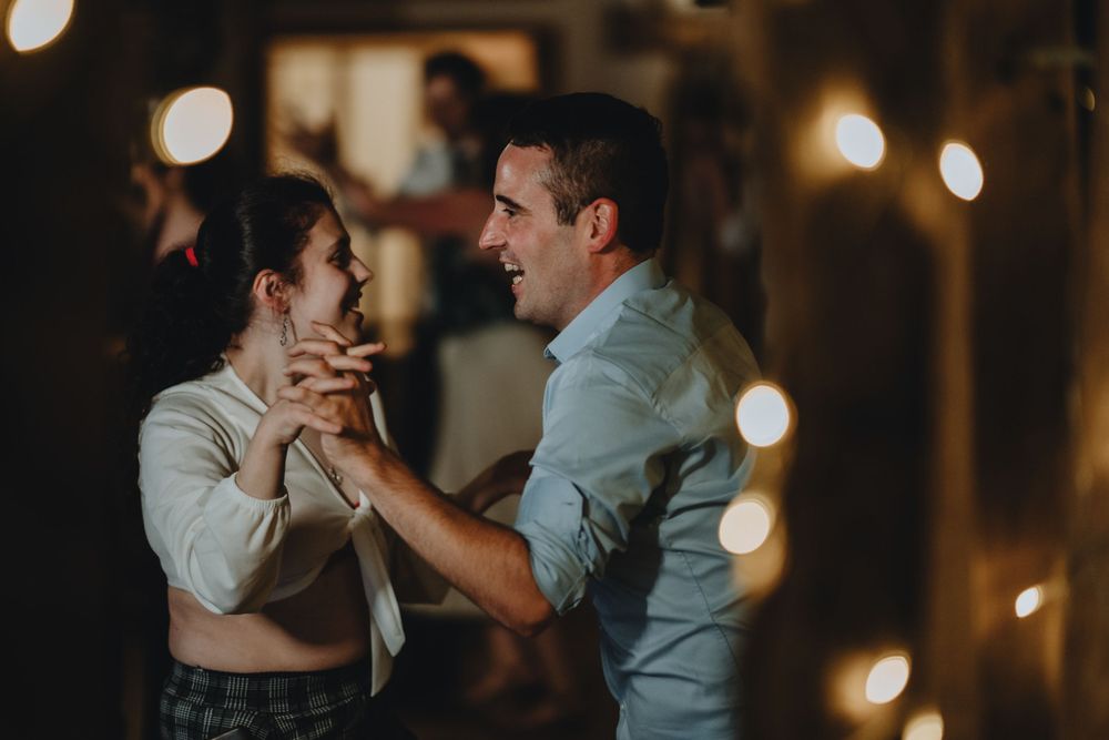 Two dancers share an intimate waltz in a dimly lit room with bokeh lights creating a romantic atmosphere.