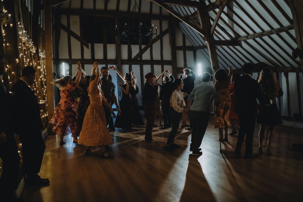 Silhouettes of people dancing on a wooden floor in a rustic barn venue decorated with string lights.