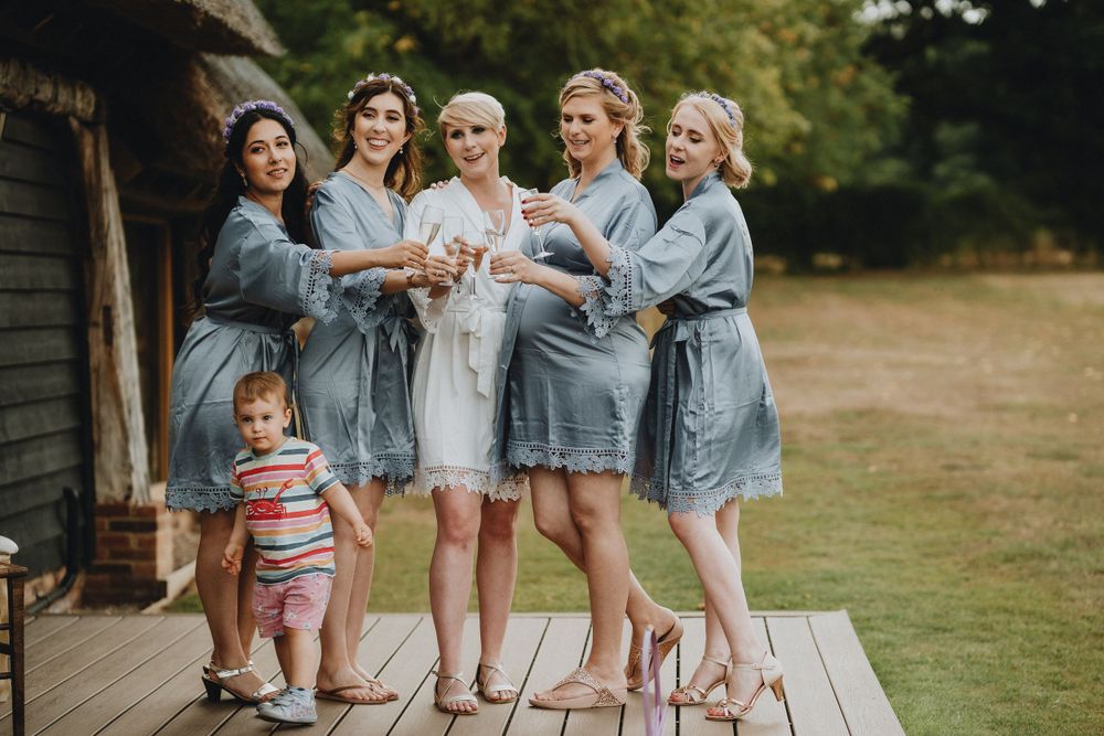 A group in matching light blue robes standing on a wooden deck toasting with champagne flutes in celebration.