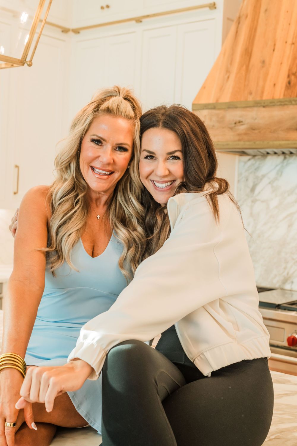 Two friends in casual attire smile warmly while sitting together in a cozy home interior.