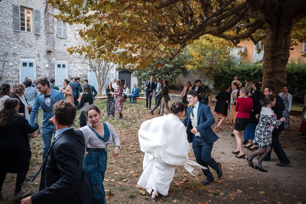Wedding guests dance and celebrate in an outdoor courtyard during an autumn reception with fallen leaves.
