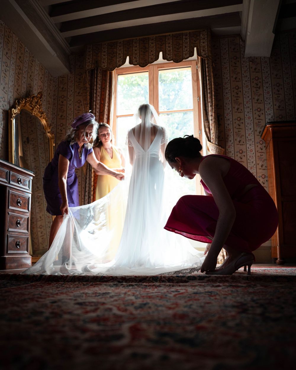 A silhouetted figure adjusts curtains in a sunlit room creating dramatic lighting and shadows on the floor.