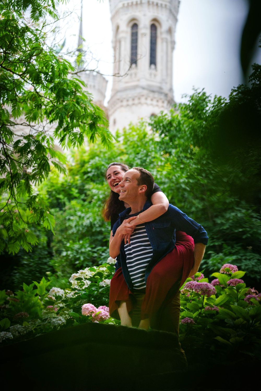 Un moment joyeux capturé dans un jardin avec des fleurs et un clocher d'église visible en arrière-plan.
