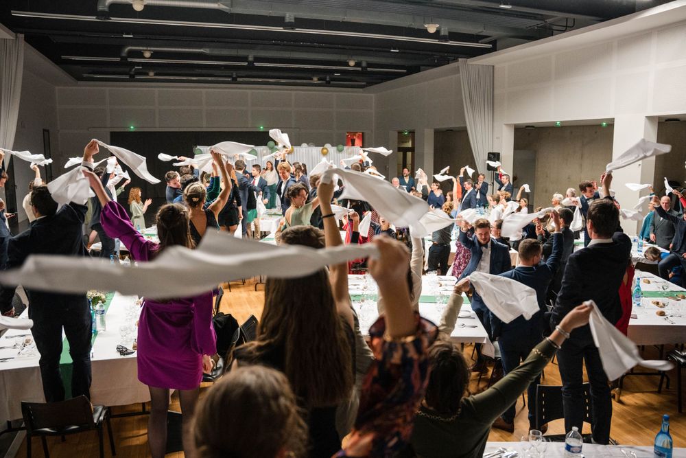 Lors d'un dîner de mariage, les invités lèvent des draps blancs dans une ambiance festive et conviviale.
