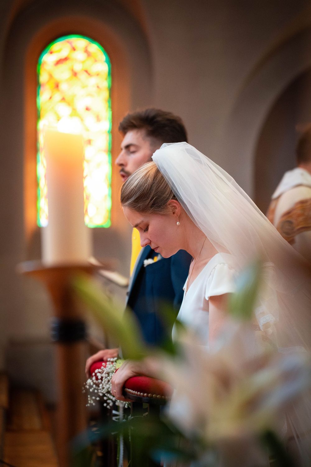A romantic wedding moment captured through stained glass windows in a church with soft natural lighting.
