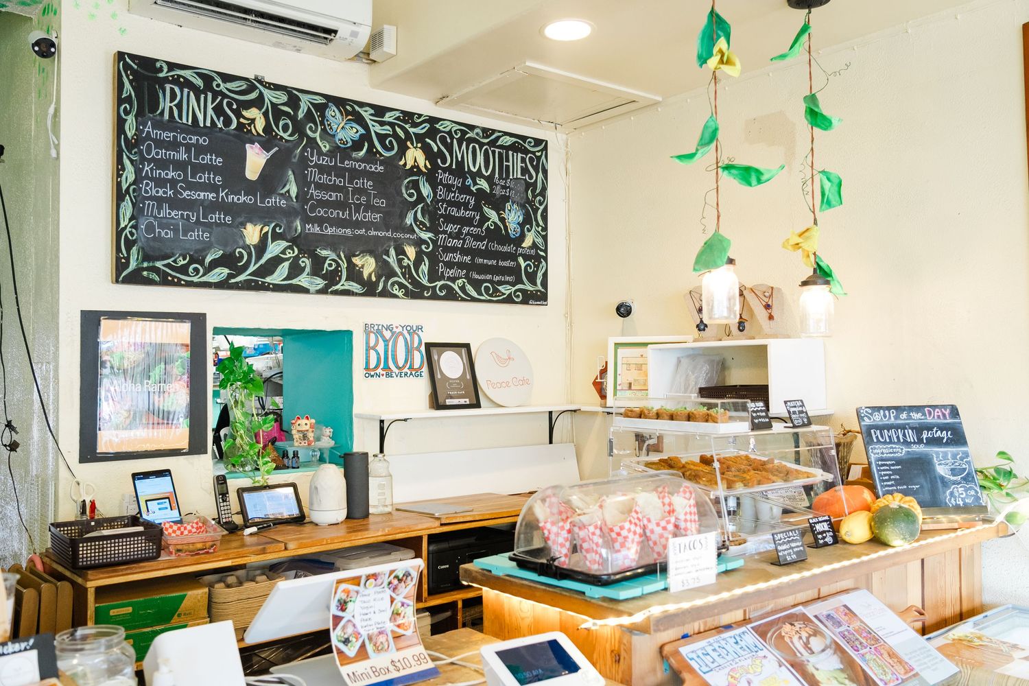A cozy cafe interior with a chalkboard menu, green decor accents, and a display counter featuring pastries and treats.