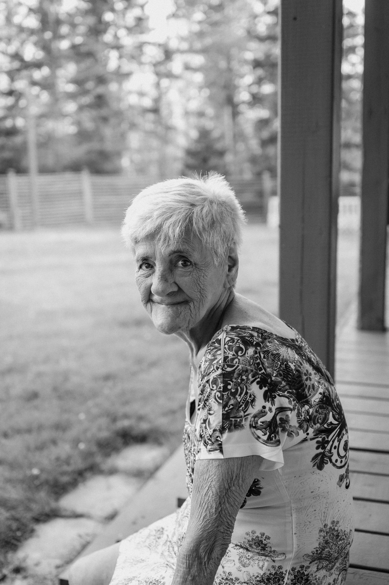 Elder sitting on porch with gentle smile in black and white portrait.