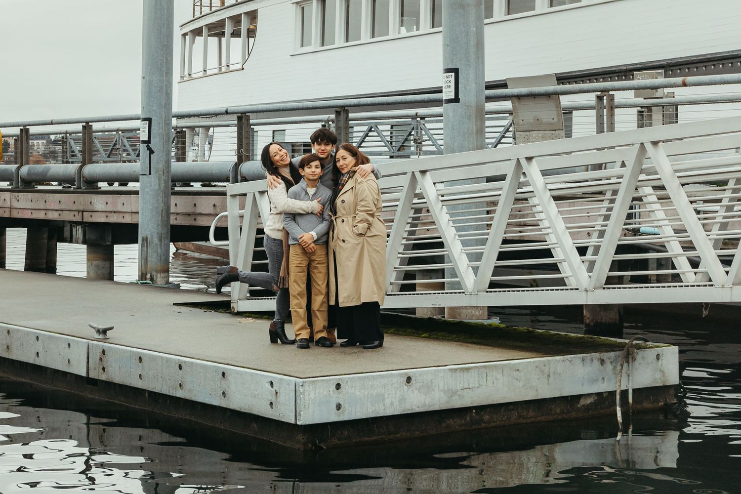 An extended family stands together on a modern floating dock platform on the waterfront near metal and glass buildings.
