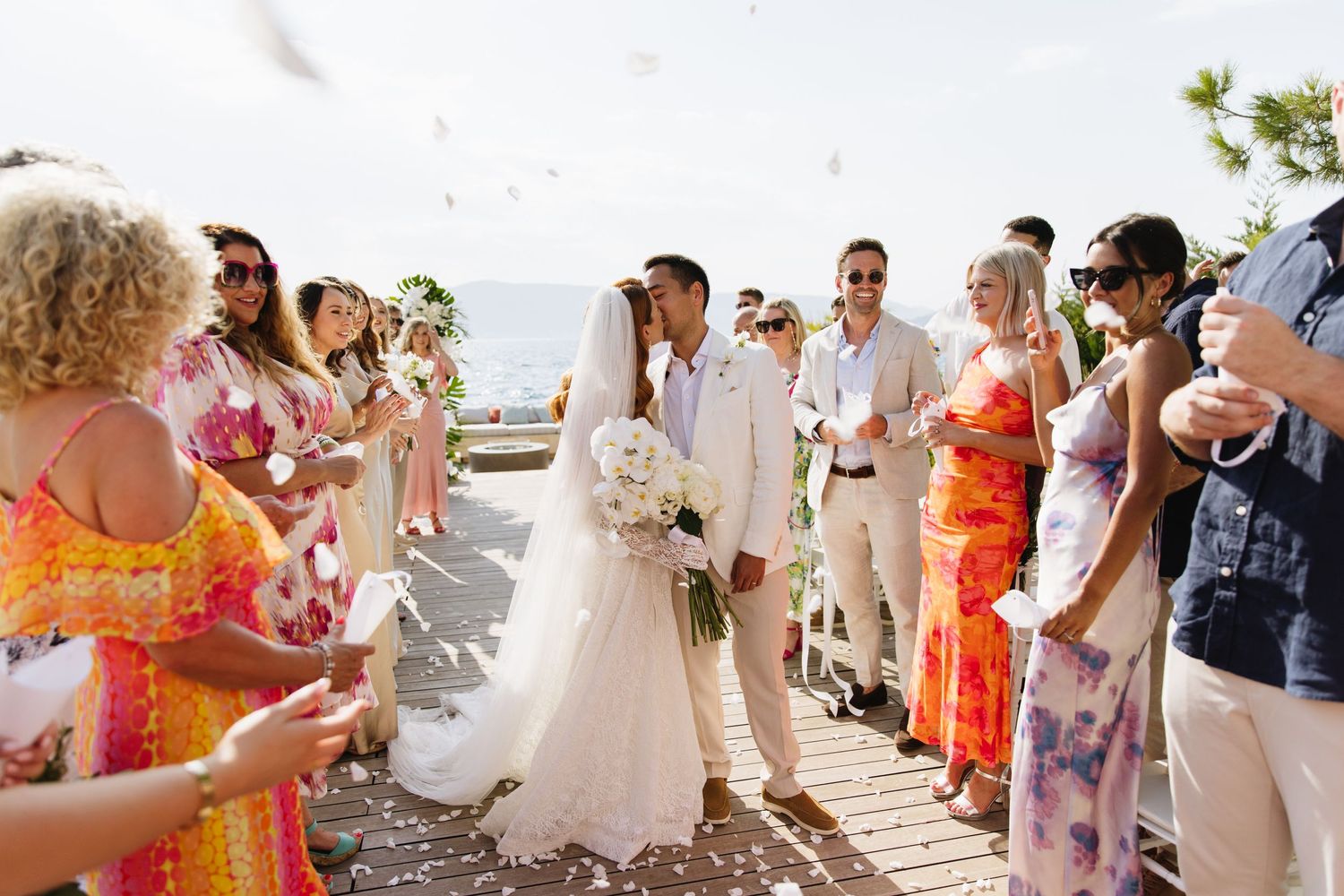 Wedding ceremony guests gather on a scenic coastal boardwalk during a bright summer celebration by the ocean.