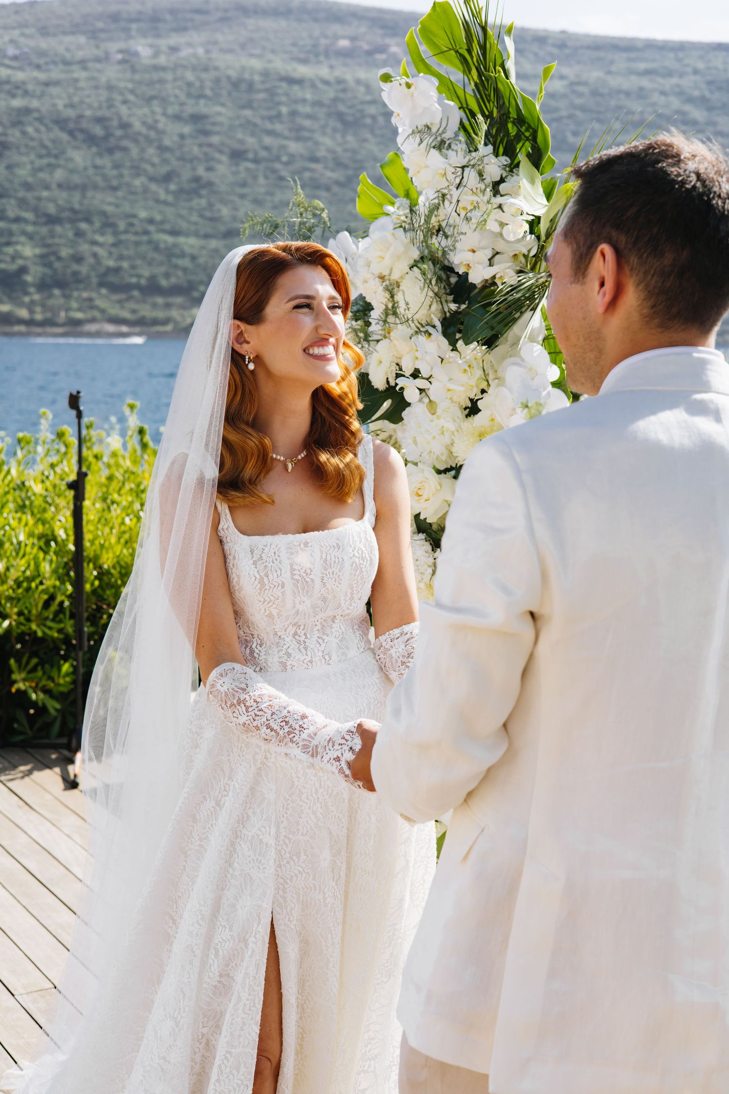 A romantic outdoor wedding ceremony overlooking a serene lake with white floral decorations and mountain views.