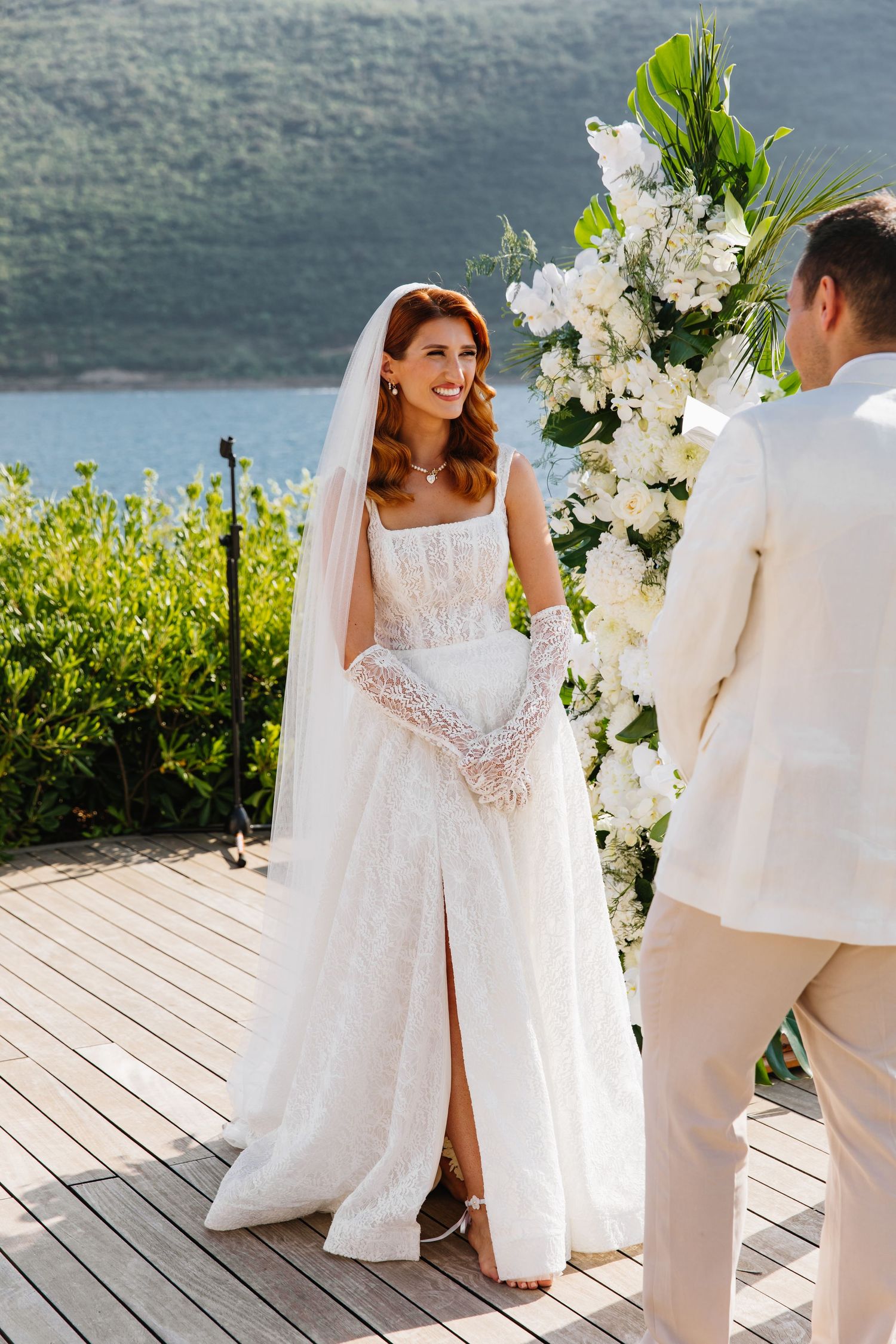 A wedding ceremony takes place on a wooden deck overlooking a scenic mountain lake with elegant white floral arrangements.