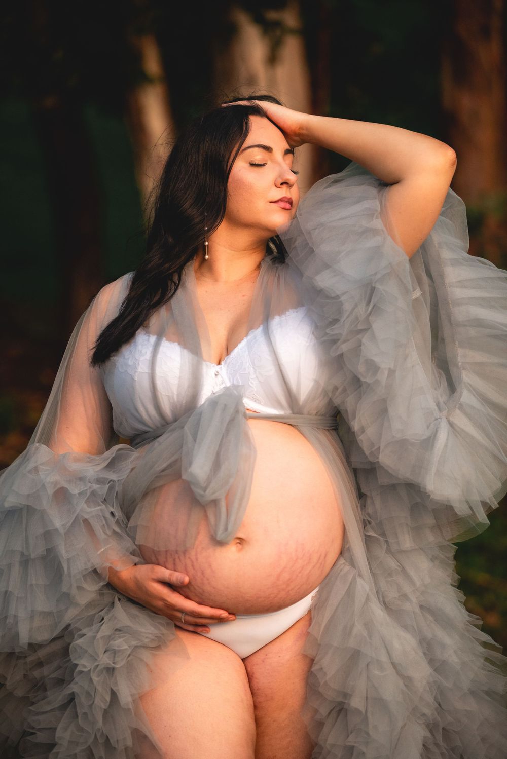 An artistic maternity portrait with flowing tulle fabric in sunlit forest.