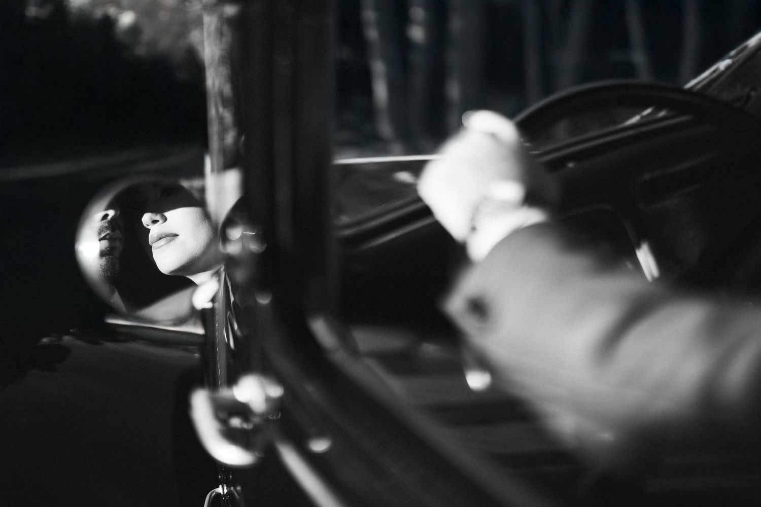 Moody black and white photo of a couple in a classic car with dramatic lighting.