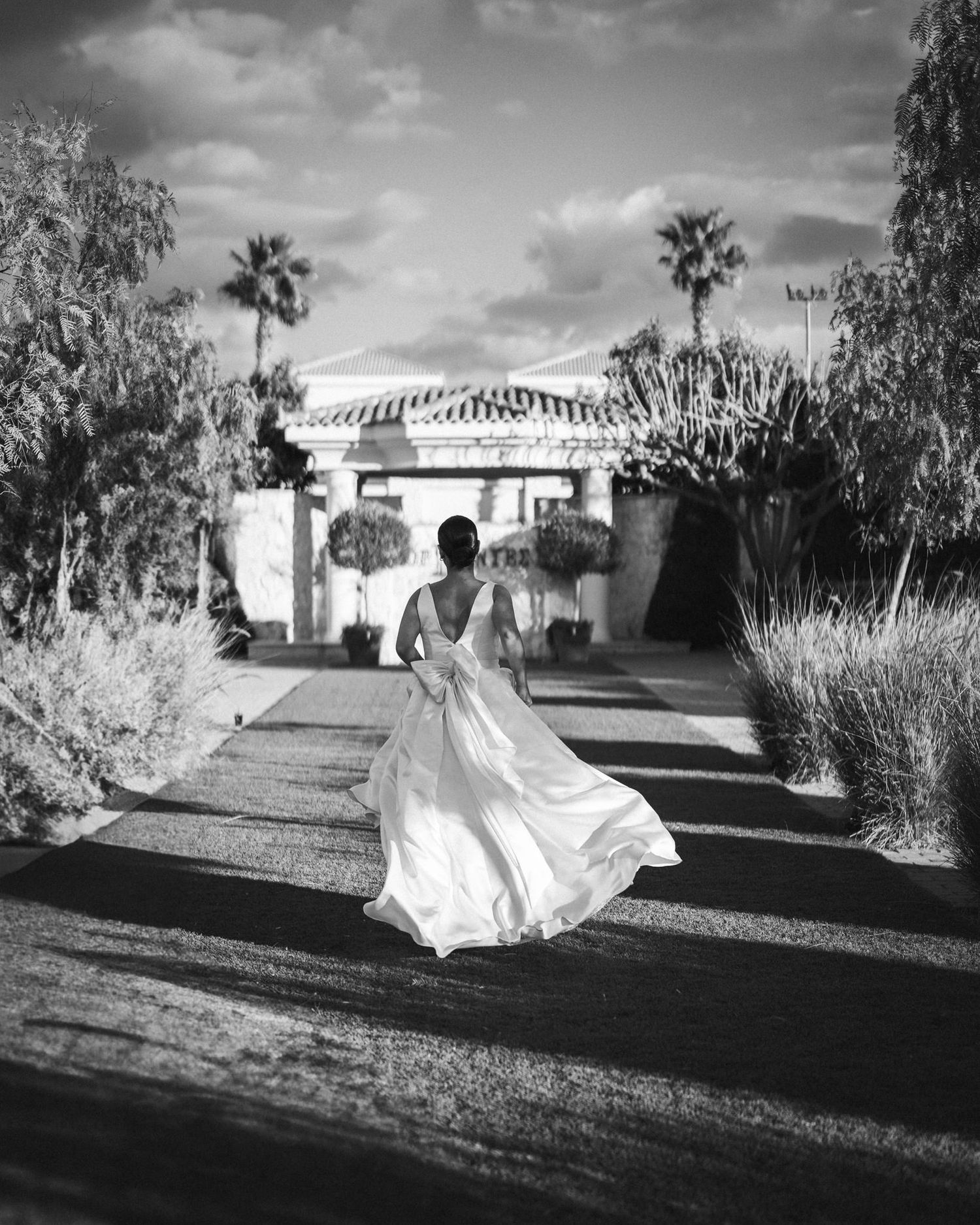 A flowing white dress dances in the wind against a dramatic black and white landscape with palm trees and buildings.