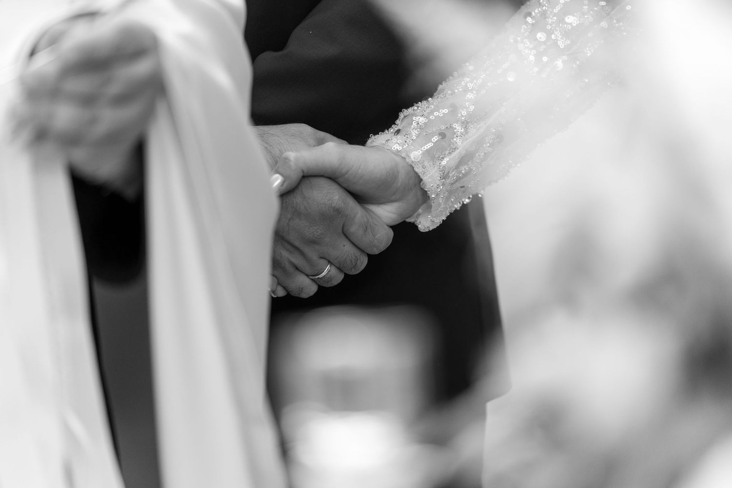 Black and white image of hands joined together during a wedding ceremony.